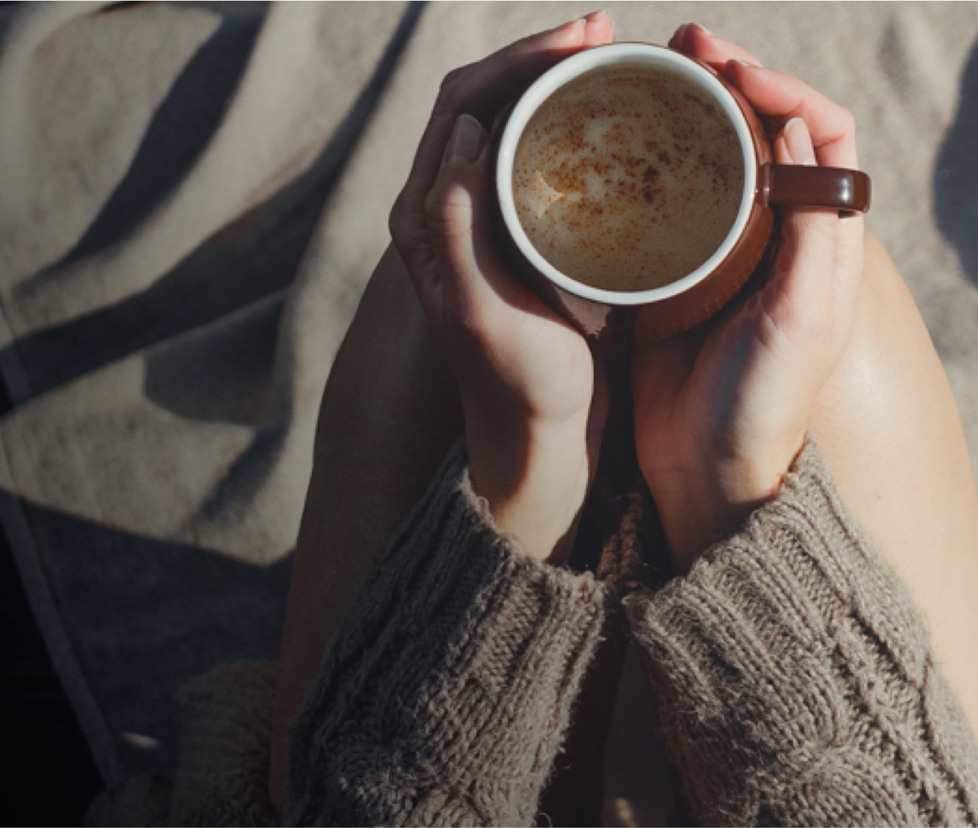 Manos sosteniendo una taza de café en un ambiente cálido y relajante, representando el estilo de vida en Calido Living.