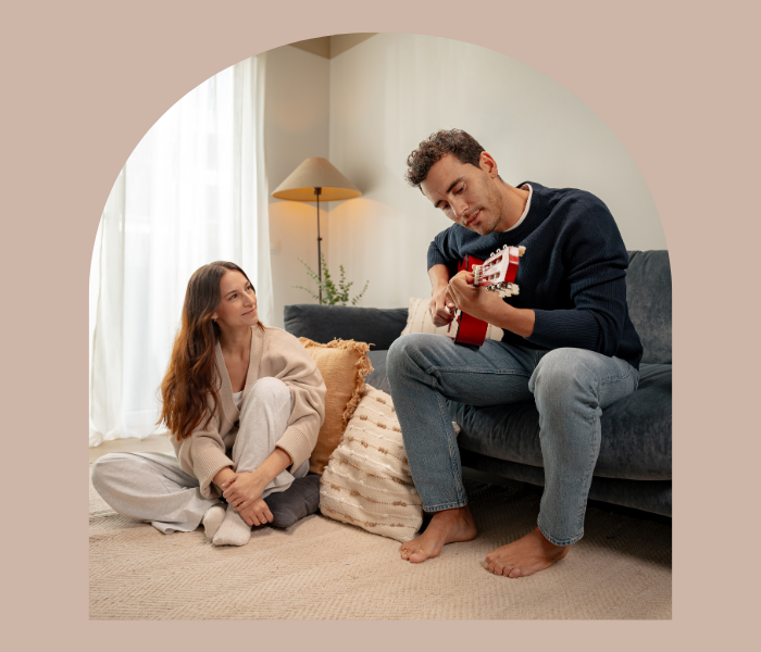 Pareja relajada en el interior de un apartamento de Calido Living, el hombre toca la guitarra y la mujer le observa.