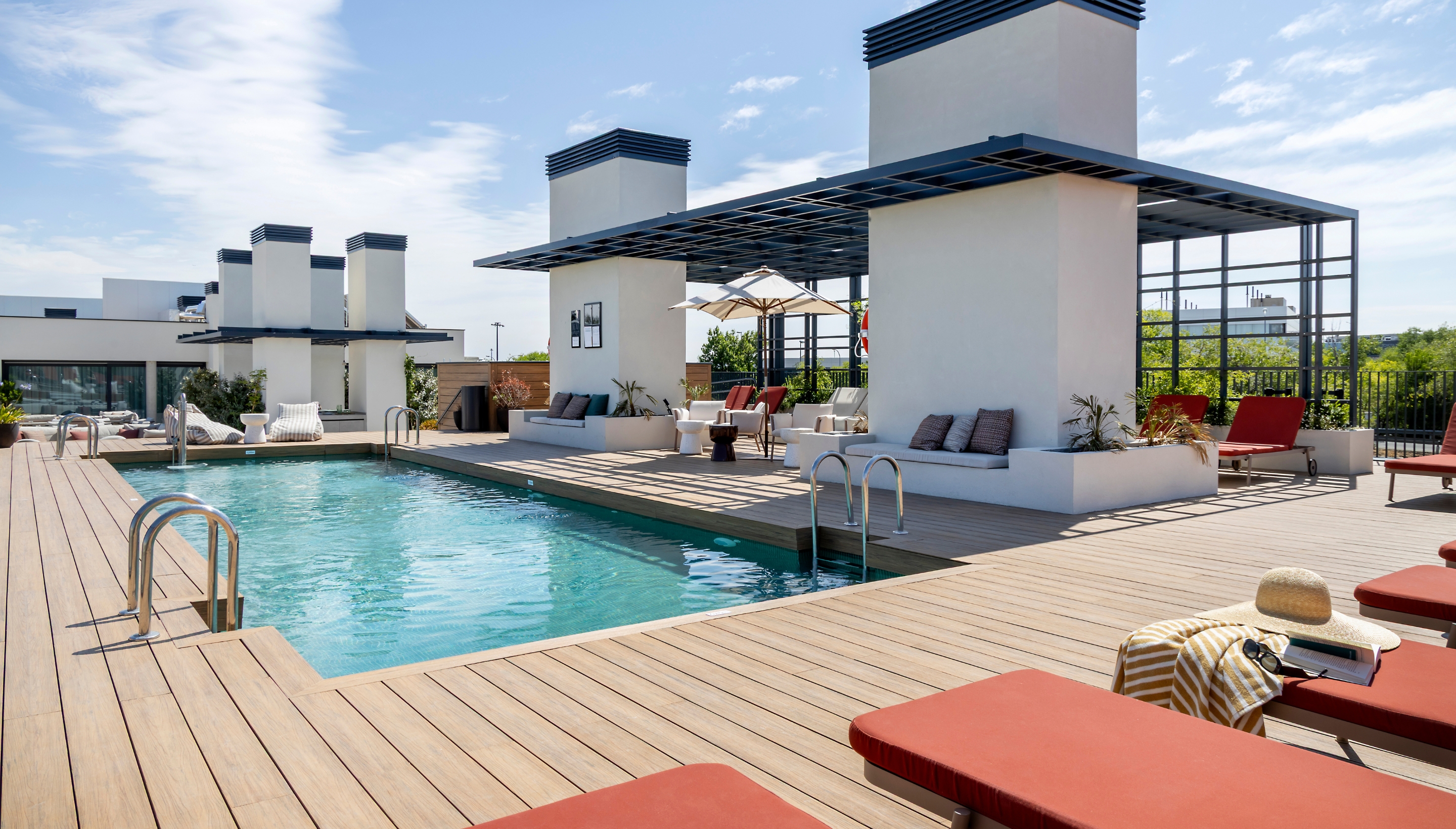 Piscina en la azotea de Calido Living, rodeada de tumbonas anaranjadas, sombrillas grandes y jardines verticales.
