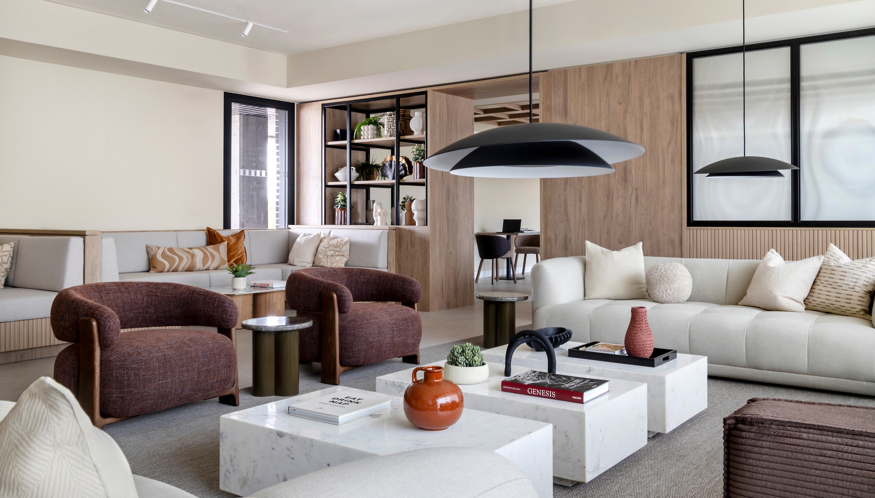 Sala común en Calido Living con diseño moderno, mesas, sillas y plantas decorativas, iluminada con luz natural.