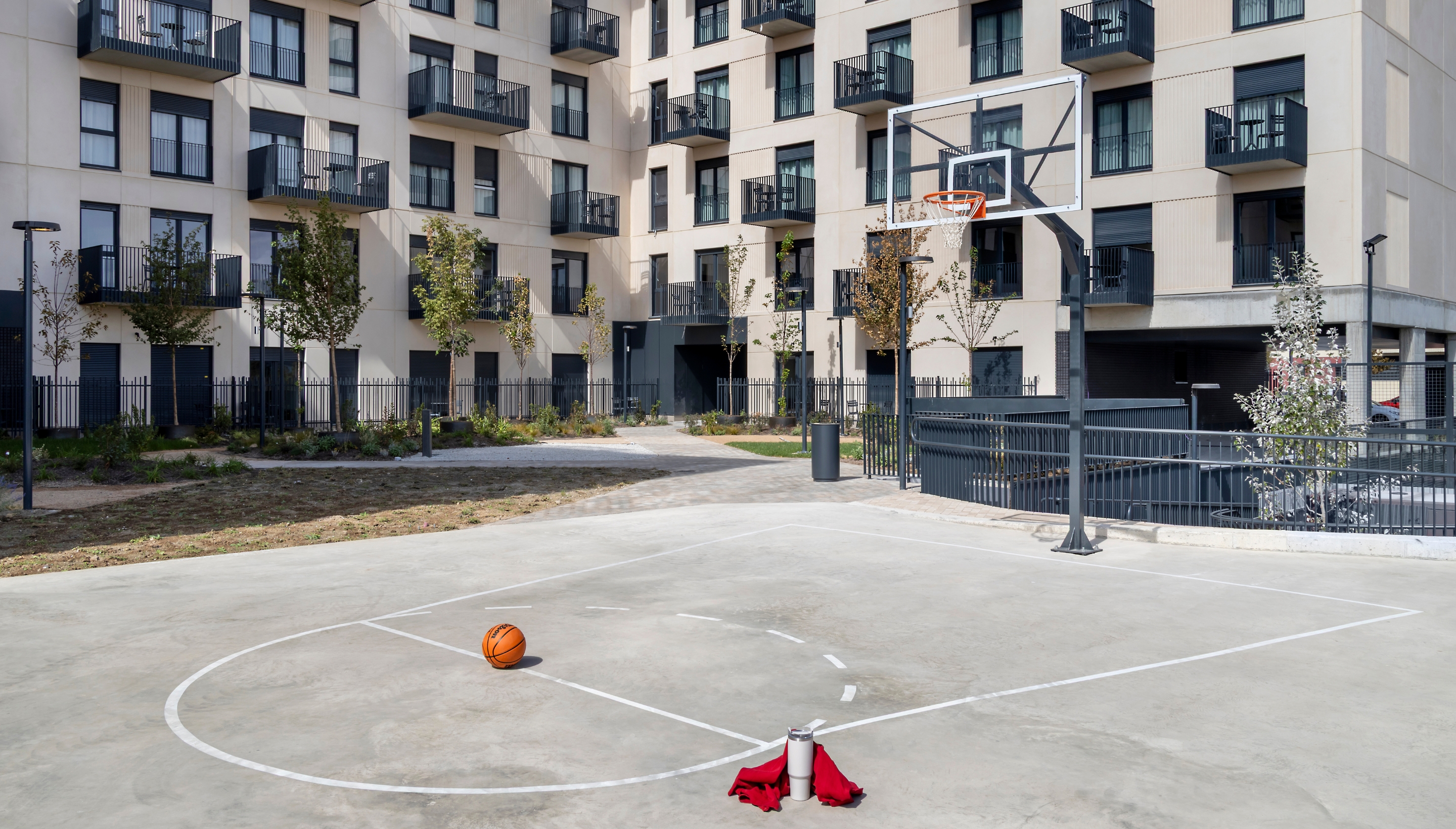 Cancha de baloncesto al aire libre en las zonas comunes de una urbanización residencial, rodeada de jardines y edificios de viviendas.