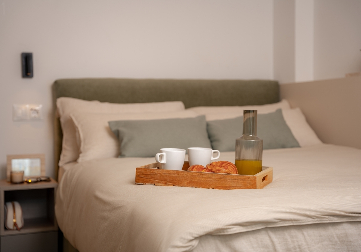 Cama con bandeja de desayuno y cojines decorativos en un estudio de Calido Living, diseñado para el confort del huésped.