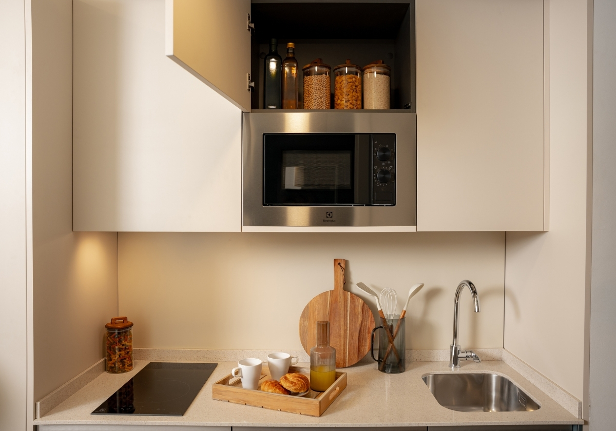 Pequeña cocina moderna con microondas, placa de inducción y espacio de almacenamiento en un estudio de Calido Living.